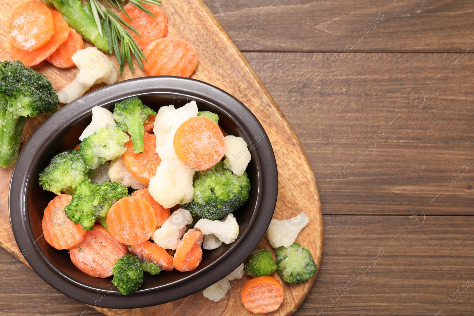 Photo of Mix of different frozen vegetables in bowl on wooden table, top view. Space for text