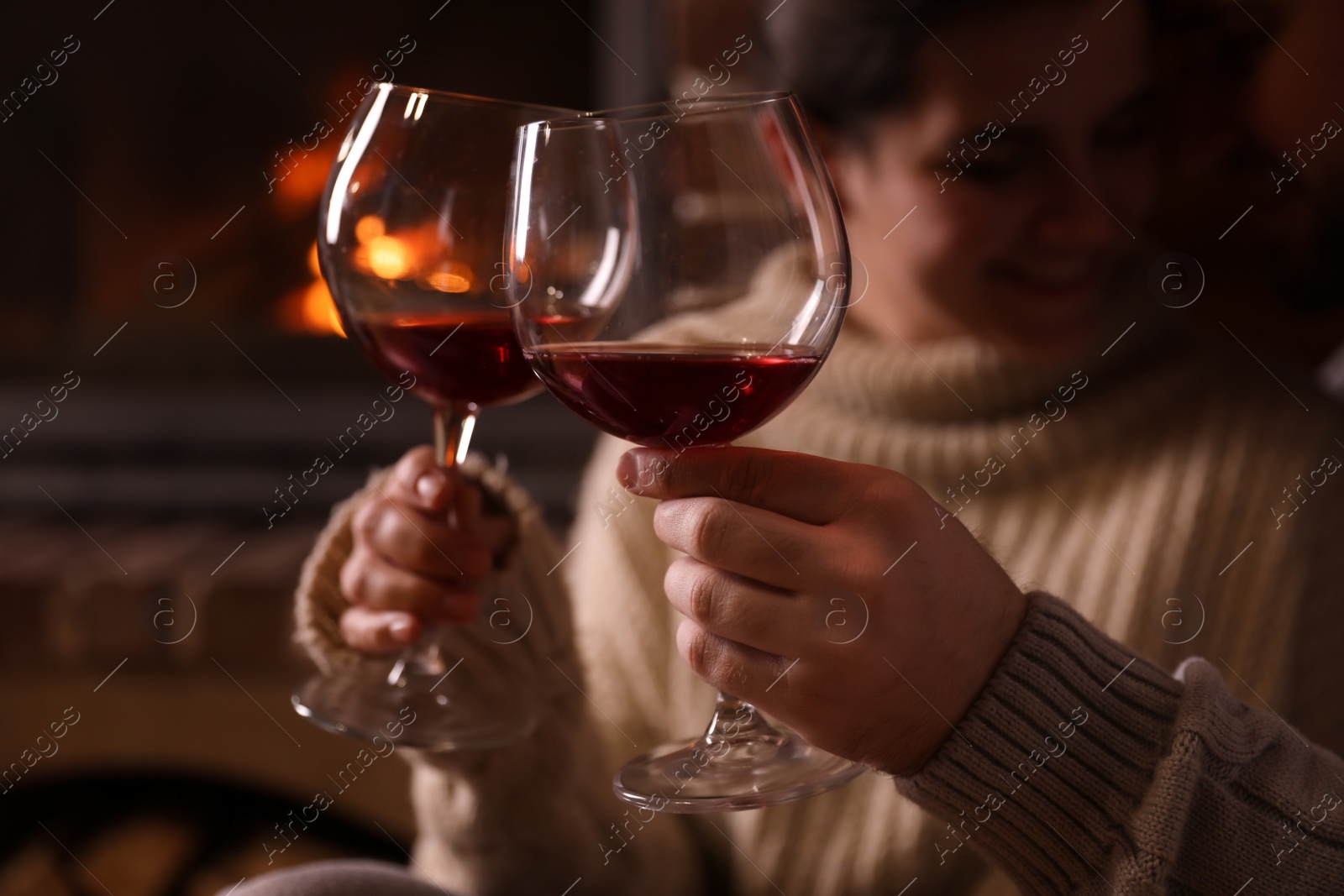 Photo of Lovely couple with glasses of wine near fireplace at home, focus on hands. Winter vacation