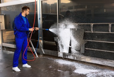 Photo of Worker cleaning auto mats with high pressure foam jet at car wash