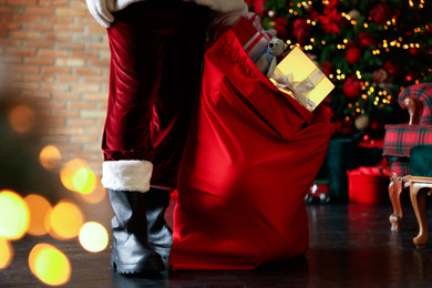 Photo of Santa Claus with bag full of Christmas gifts against blurred festive lights, closeup