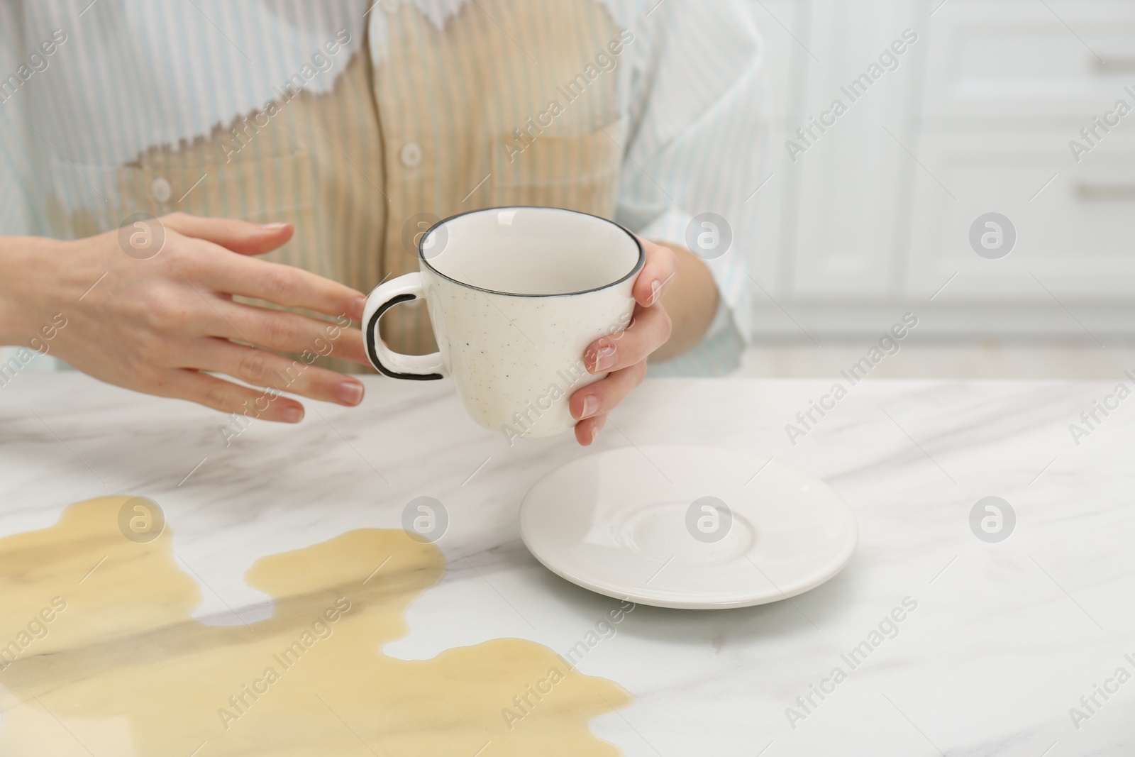 Photo of Woman with spilled coffee over her shirt at marble table indoors, closeup