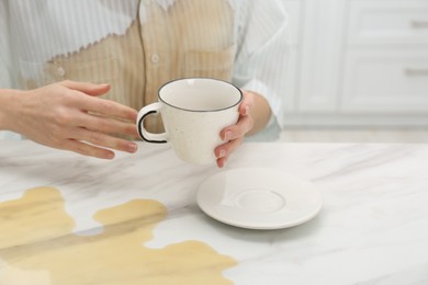 Photo of Woman with spilled coffee over her shirt at marble table indoors, closeup