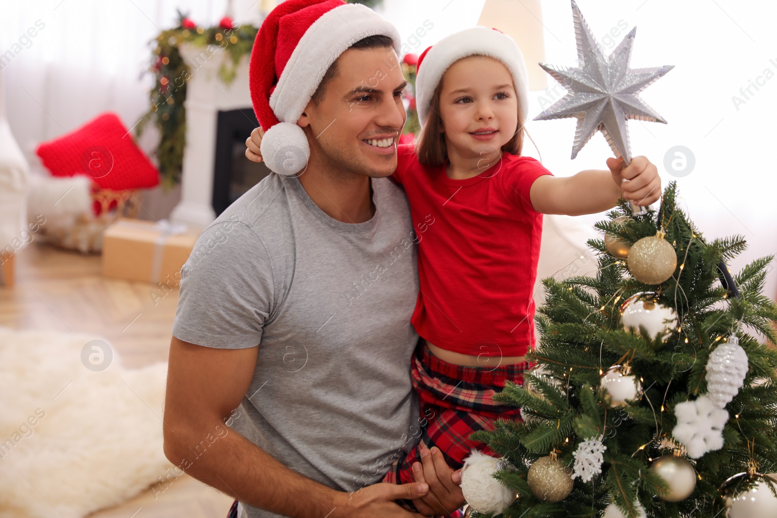 Photo of Father and little daughter decorating Christmas tree with star topper in room