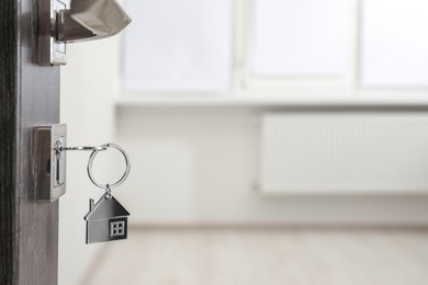 Photo of Mortgage and real estate. Open door with key and house shaped keychain against blurred background, space for text