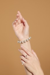 Photo of Young woman wearing elegant pearl jewelry on brown background, closeup