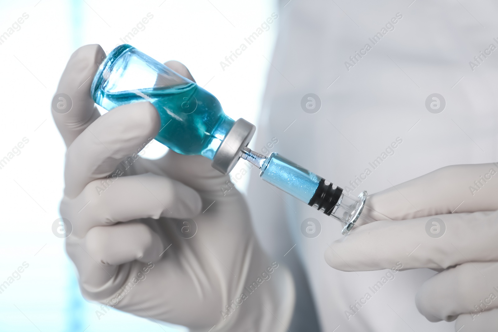 Photo of Doctor filling syringe with vaccine from vial on blurred background, closeup