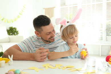 Happy son with bunny ears headband and his father painting Easter egg at home