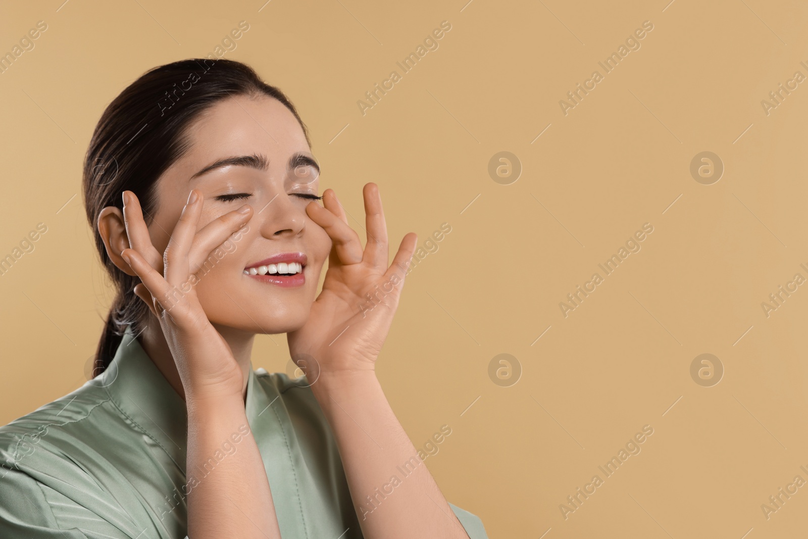 Photo of Young woman massaging her face on beige background. Space for text