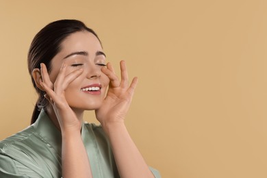 Young woman massaging her face on beige background. Space for text