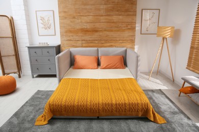 Photo of Room interior with sofa unfolded into bed near wooden wall