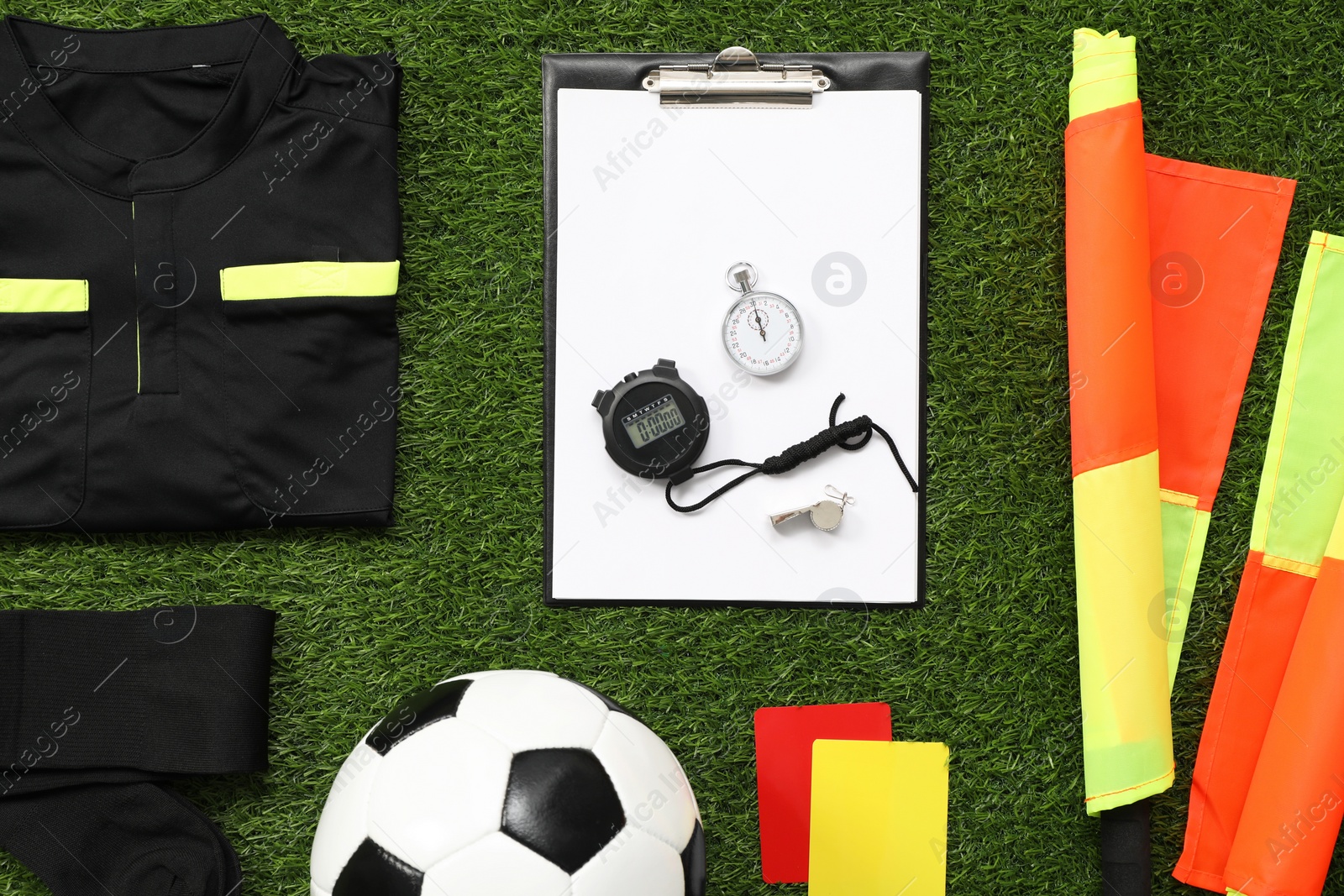 Photo of Uniform, soccer ball and other referee equipment on green grass, flat lay