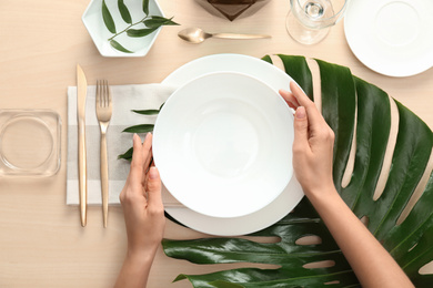 Woman setting table with green leaves for festive dinner, top view