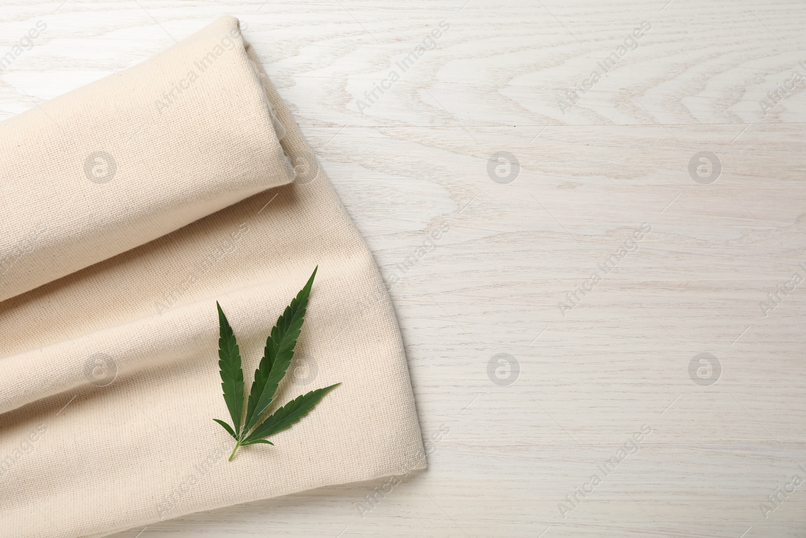 Photo of Hemp cloth with green leaf on white wooden table, top view. Space for text