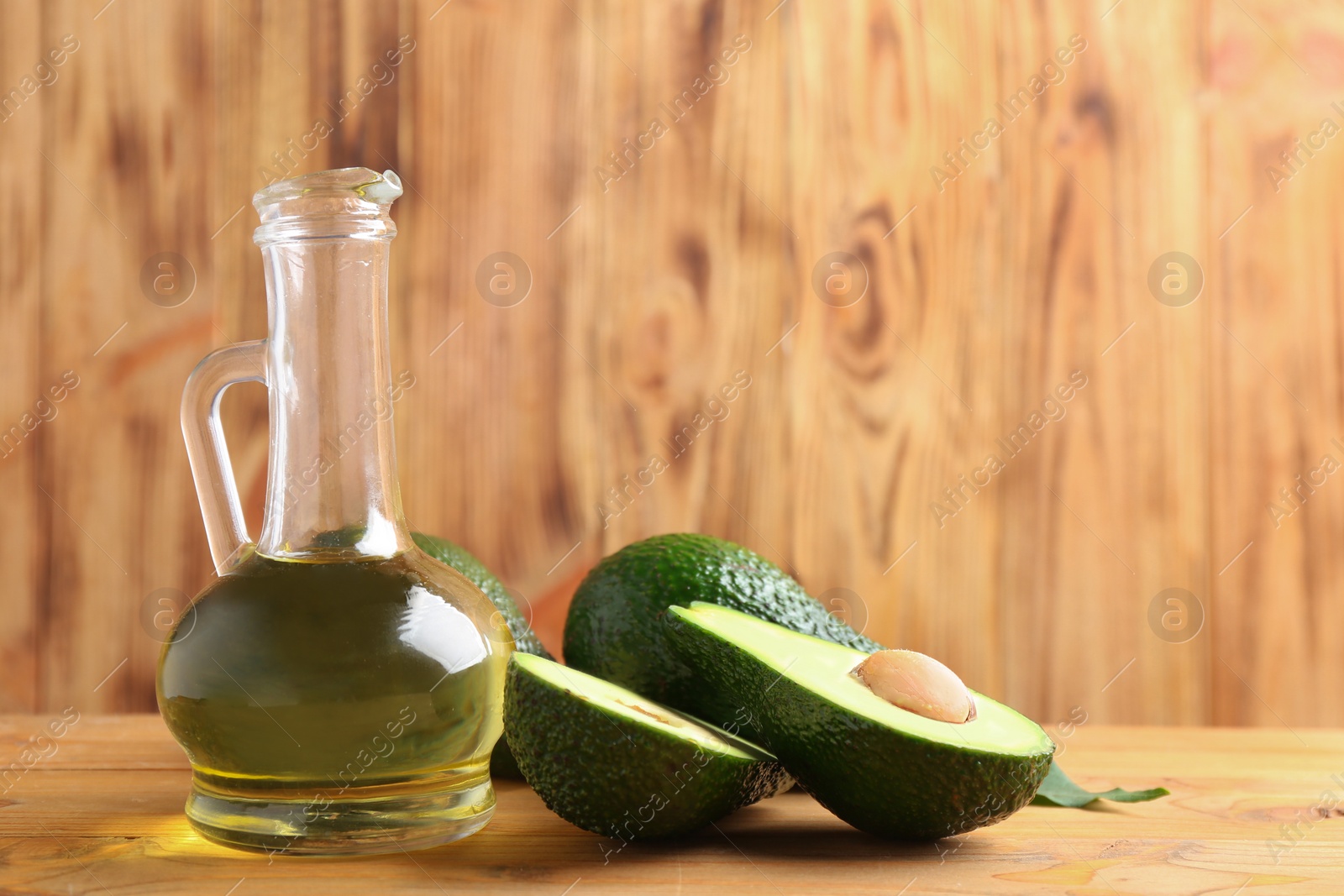 Photo of Pitcher of natural oil and avocados on table against wooden background. Space for text