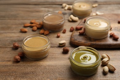 Photo of Jars with butters made of different nuts and ingredients on wooden table, closeup