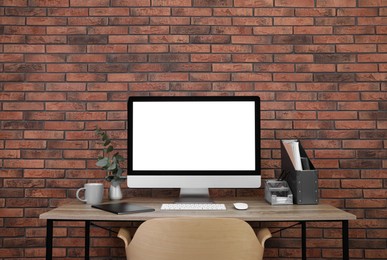 Photo of Modern computer with blank screen on desk near brick wall, space for design. Comfortable workplace