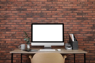 Modern computer with blank screen on desk near brick wall, space for design. Comfortable workplace