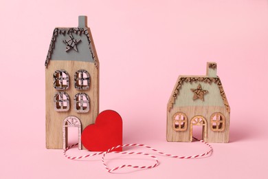 Photo of Decorative heart and cord between two house models on pink background symbolizing connection in long-distance relationship