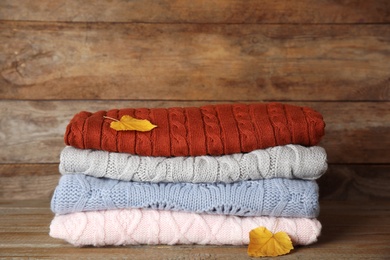 Photo of Stack of warm knitted clothes and autumn leaves on wooden background