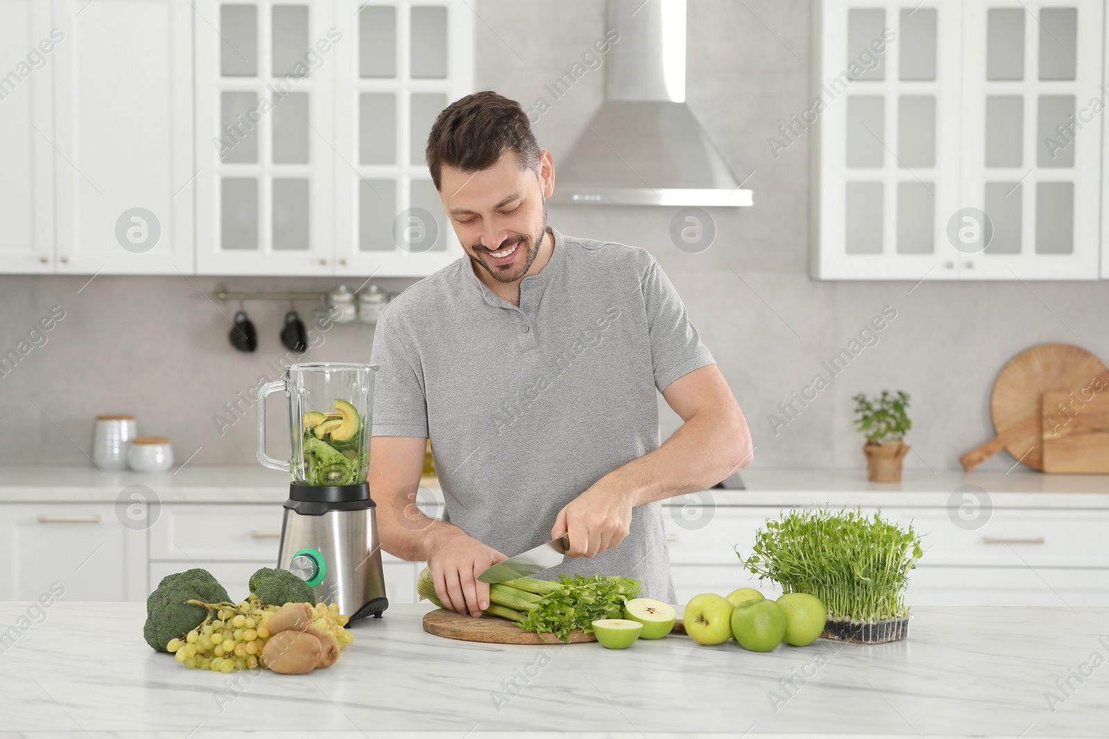 Photo of Happy man cutting celery for delicious smoothie at white marble table in kitchen