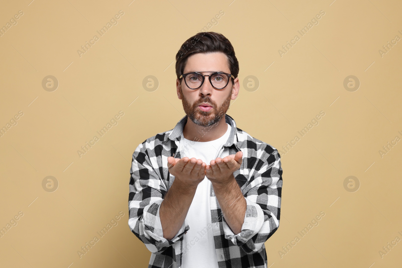 Photo of Handsome man blowing kiss on beige background