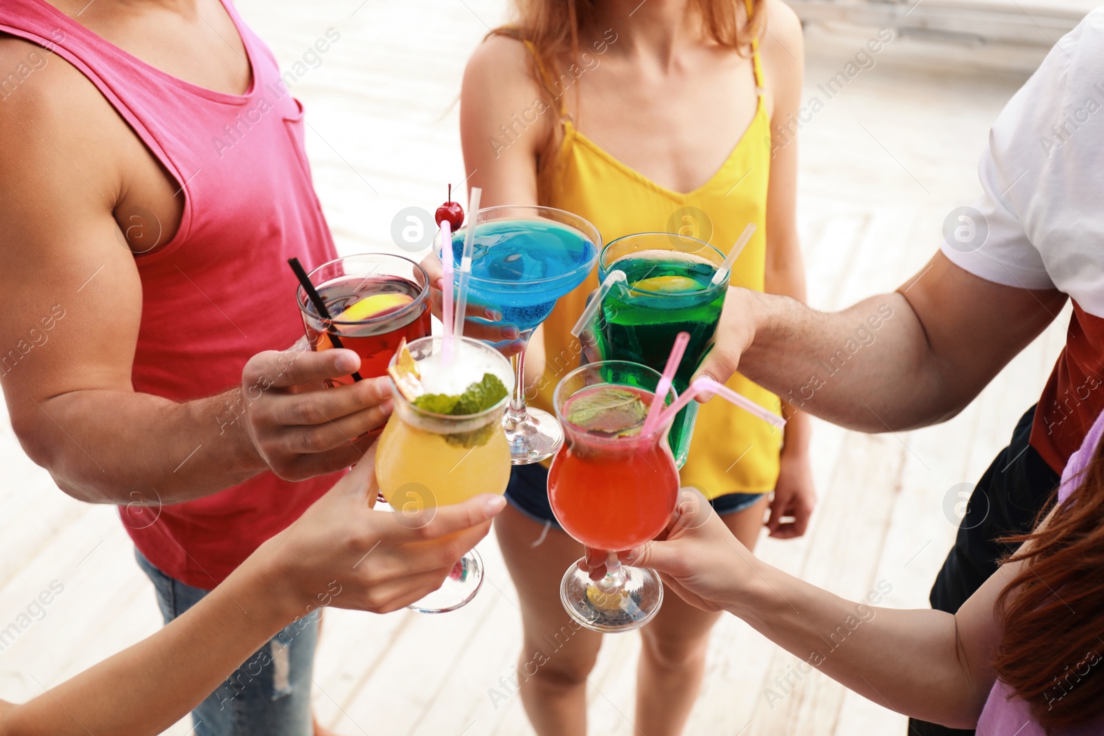 Photo of Friends clinking glasses with fresh summer cocktails outdoors, closeup
