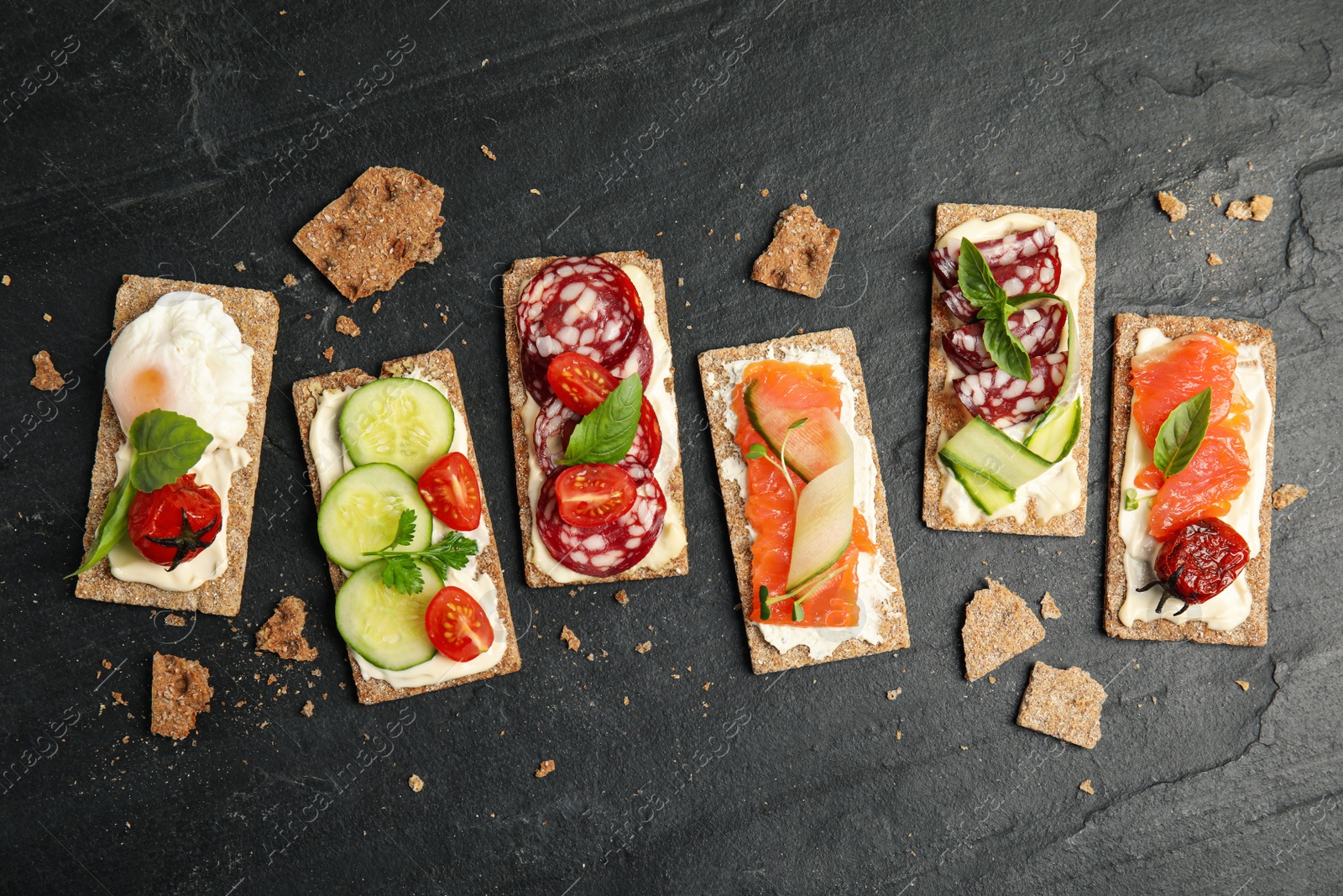 Photo of Fresh rye crispbreads with different toppings on black table, flat lay