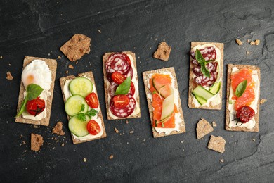 Photo of Fresh rye crispbreads with different toppings on black table, flat lay
