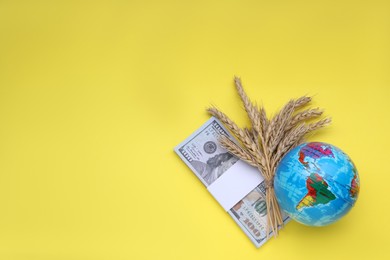 Photo of Import and export concept. Globe, ears of wheat and money on yellow background, flat lay with space for text