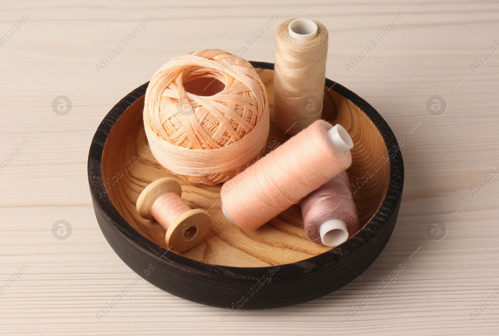 Photo of Bowl with color sewing threads on wooden table