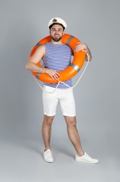 Happy sailor with ring buoy on light grey background