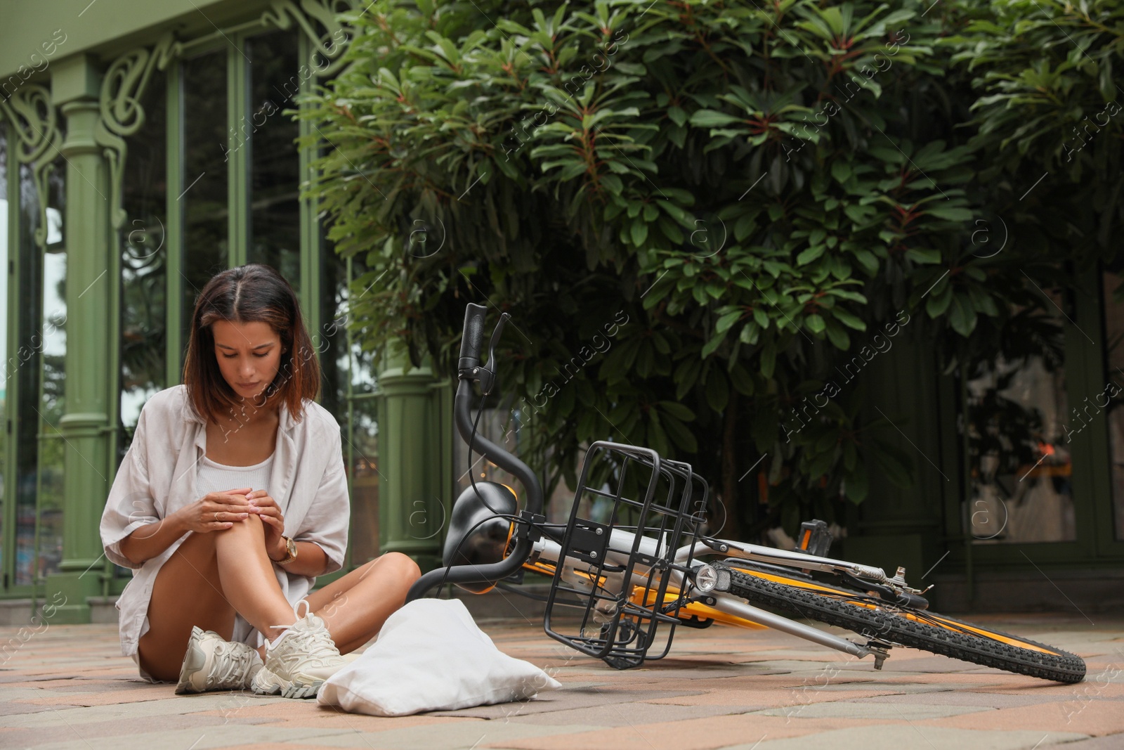 Photo of Young woman with injured knee near bicycle on city street. Space for text