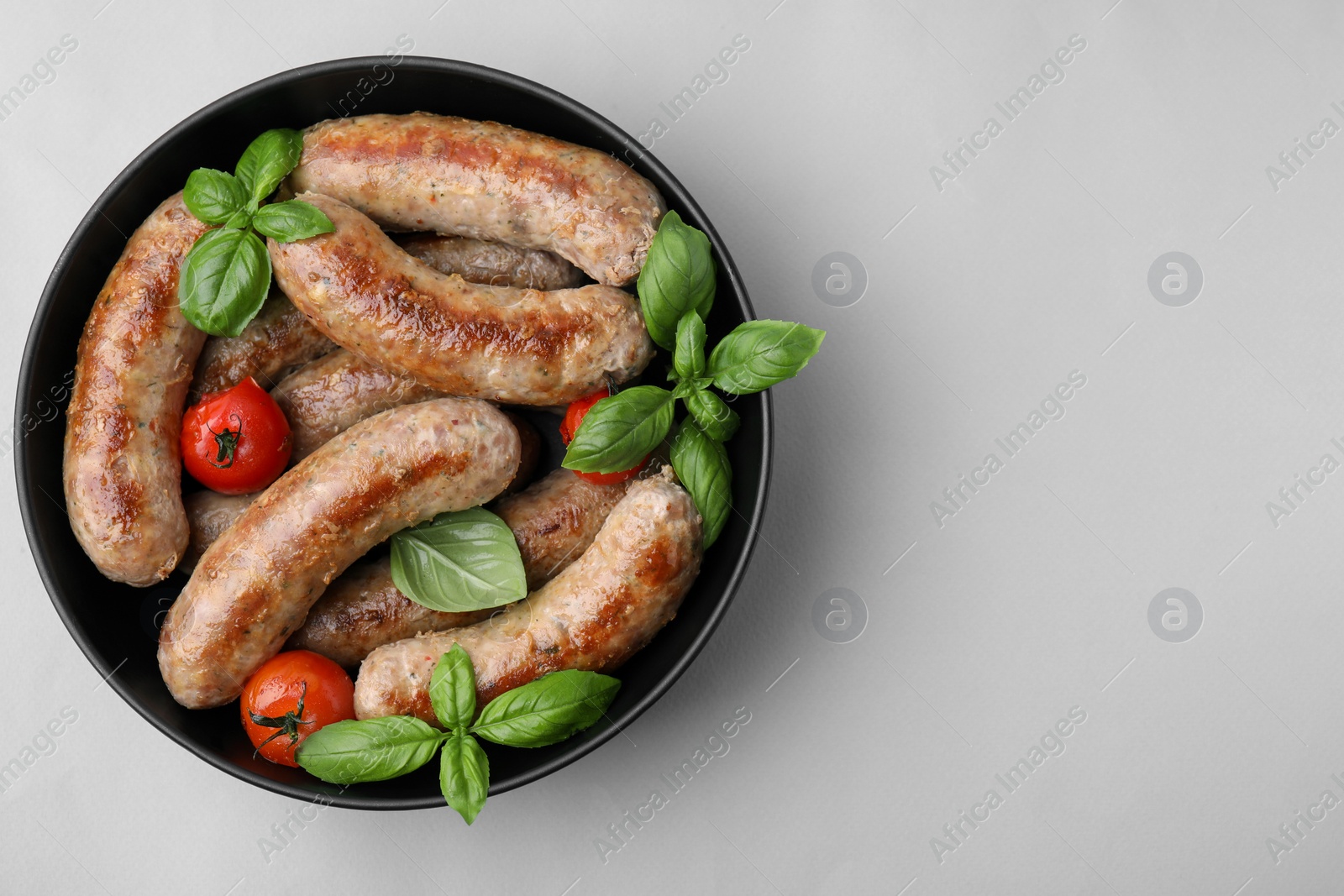 Photo of Bowl with tasty homemade sausages, basil leaves and tomatoes on grey table, top view. Space for text