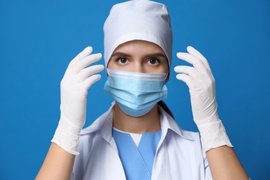 Doctor in protective mask and medical gloves against blue background