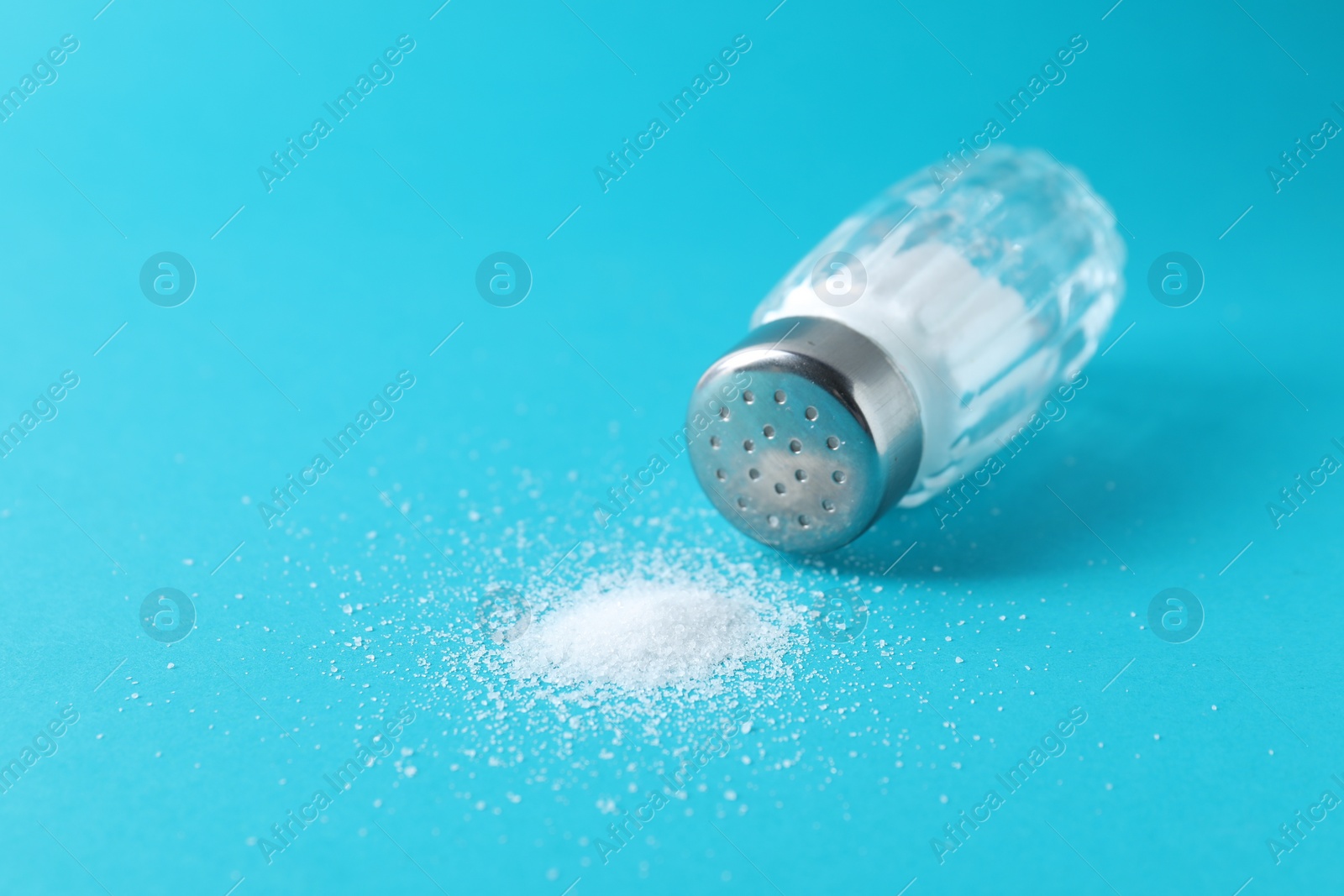 Photo of Organic white salt in glass shaker on light blue background, closeup. Space for text