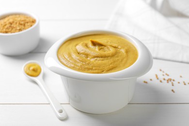 Photo of Tasty mustard sauce in bowl on white wooden table, closeup