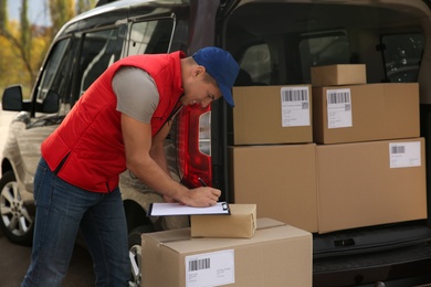 Courier with clipboard checking packages near car outdoors