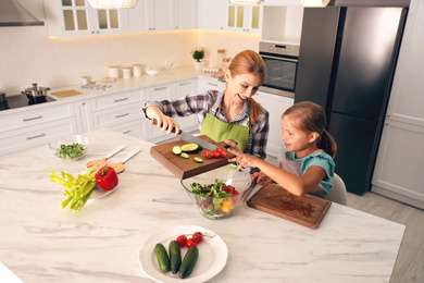 Photo of Mother and daughter cooking salad together in kitchen