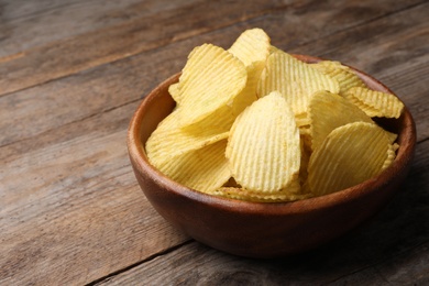 Photo of Delicious crispy potato chips in bowl on table, space for text