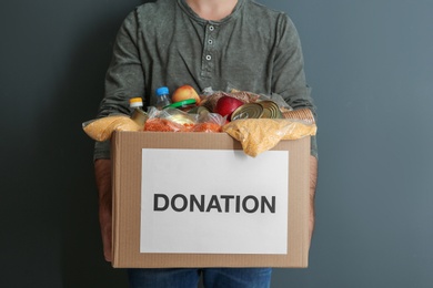 Photo of Man holding donation box with food on gray background, closeup