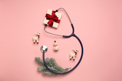 Photo of Greeting card for doctor with stethoscope, gift box and Christmas decor on pink background, flat lay