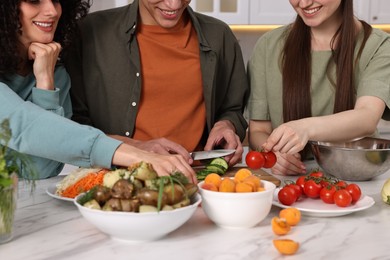 Photo of Friends cooking healthy vegetarian meal at white marble table in kitchen, closeup