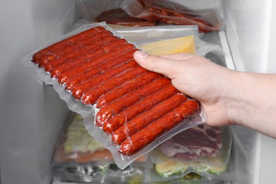Photo of Woman putting vacuum bag with sausages into fridge, closeup. Food storage