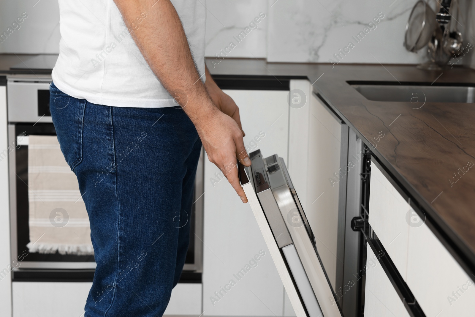 Photo of Man opening dishwasher's door in kitchen, closeup