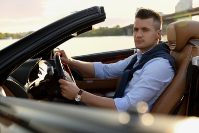 Stylish man driving luxury convertible car outdoors