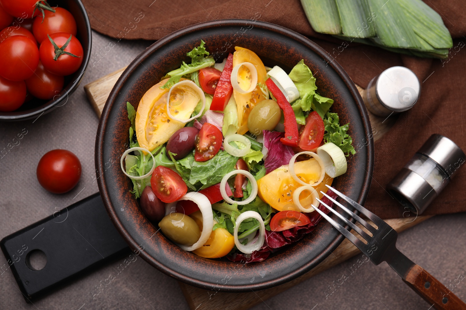 Photo of Bowl of tasty salad with leek and olives served on brown table, flat lay