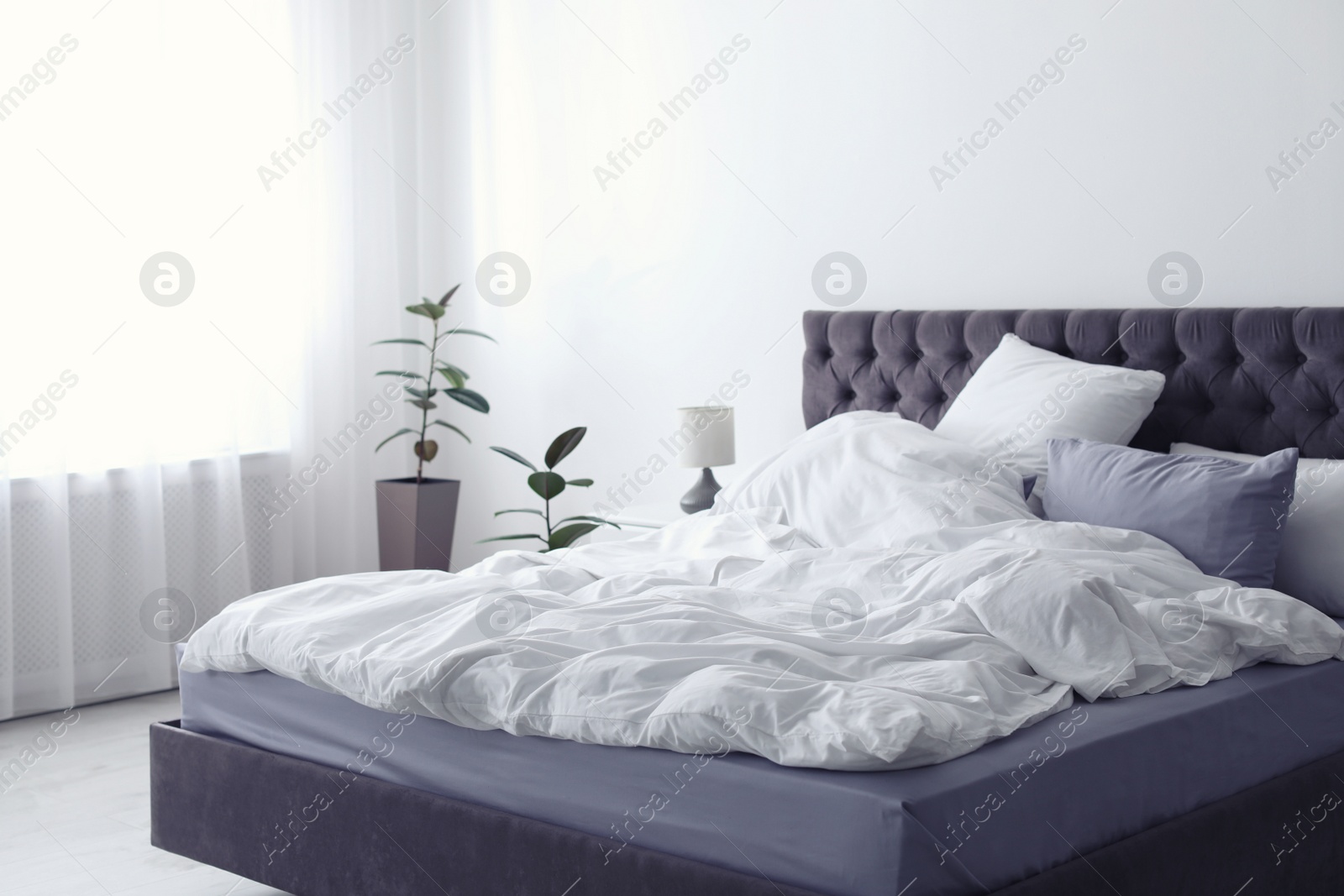 Photo of Modern bed with crumpled blanket and pillows indoors