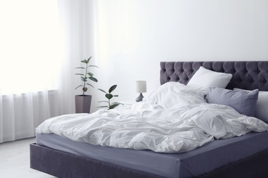 Modern bed with crumpled blanket and pillows indoors