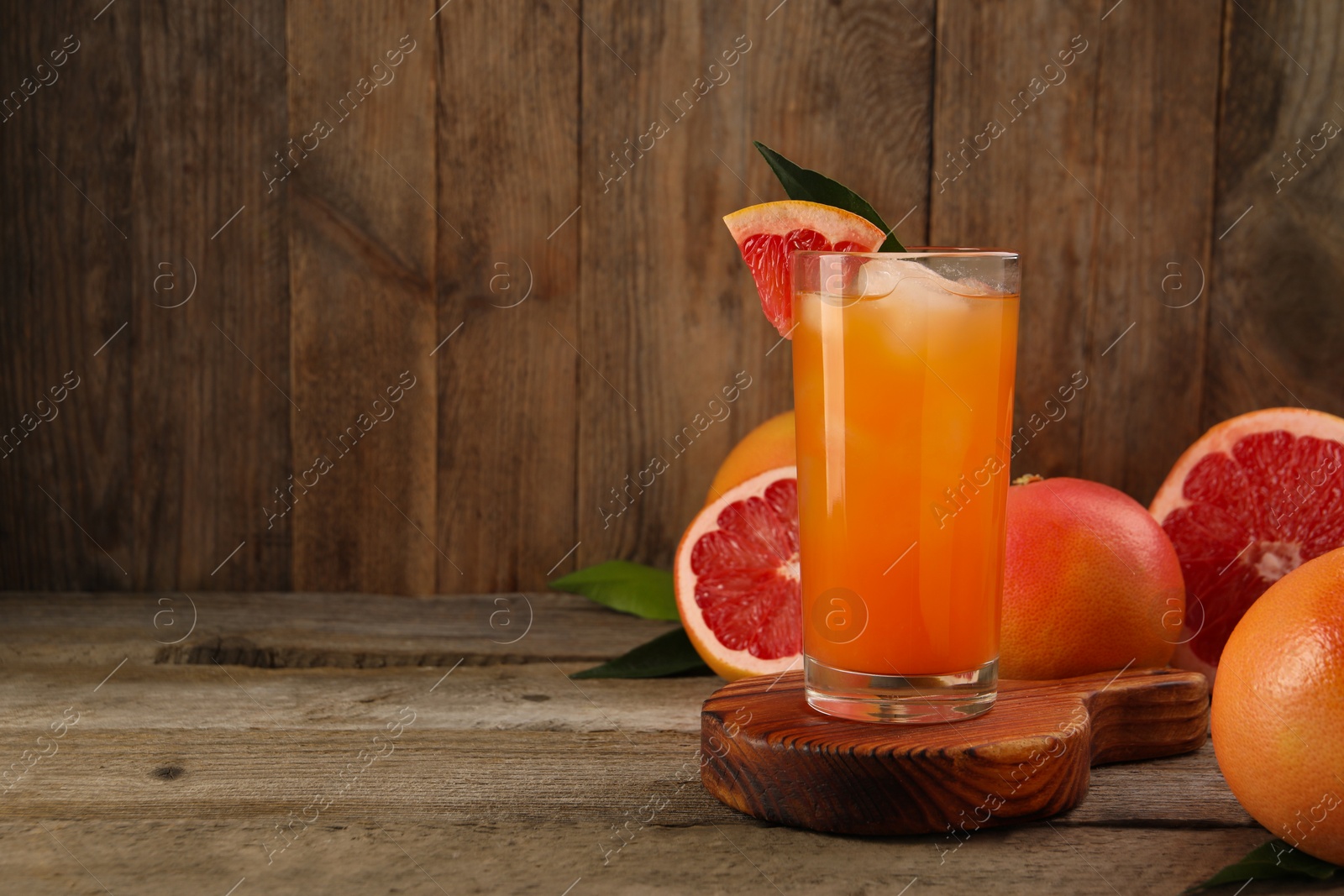 Photo of Tasty grapefruit drink with ice in glass and fresh fruits on wooden table. Space for text