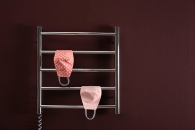 Photo of Modern heated towel rail with cloth face masks on dark wall. Space for text